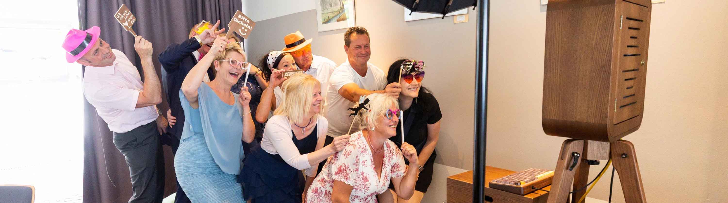 Gäste mit Holz-Requisiten lachen vor der Nussbaum-Lachbox auf einer Feier